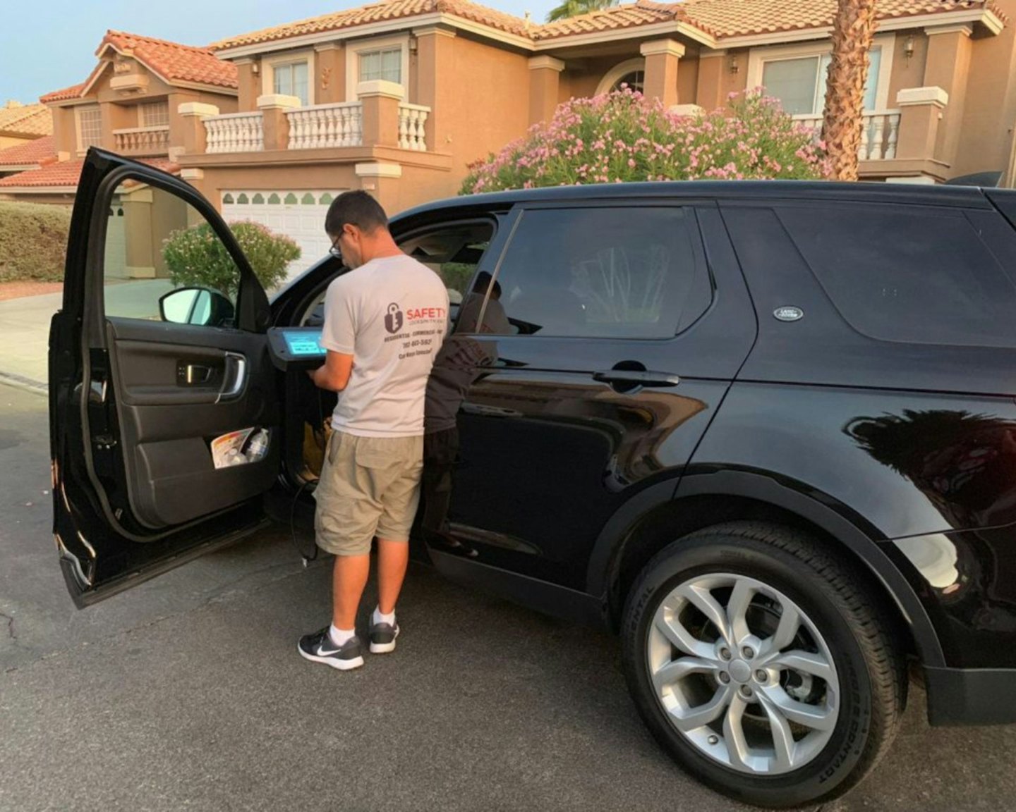 Cerrajero programando llave de coche en el panel de la puerta de un SUV al anochecer.