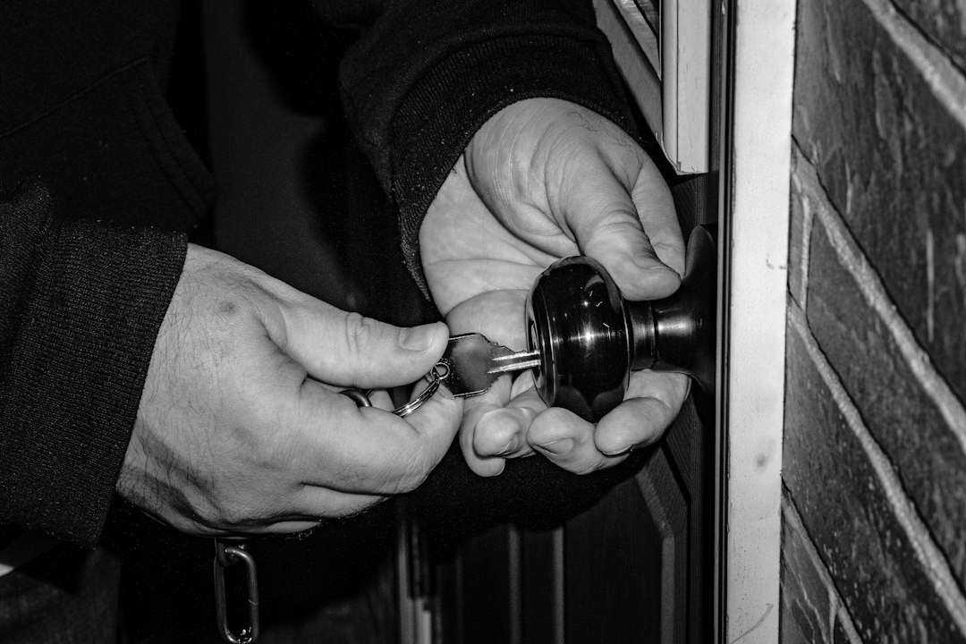 Hands inserting a key into a dark doorknob.